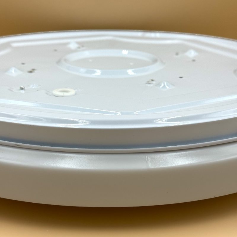 Close-up of a white circular smart speaker top with a central recessed area and small control marks.