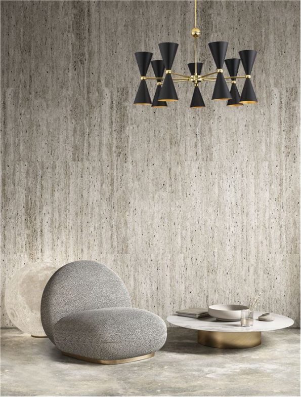 Modern living room corner with a gray rounded lounge chair, a white marble coffee table on a gold base, and a black-and-gold chandelier against a concrete wall.