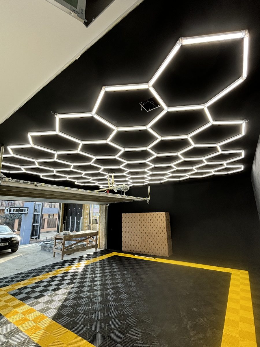 Geometric honeycomb ceiling lights forming a pattern over a dark room with a checkered yellow and black floor edge