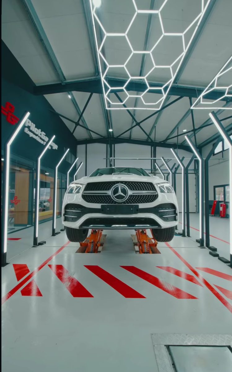 White Mercedes SUV on a lift in a modern auto workshop with hexagonal neon ceiling lights and red floor markings