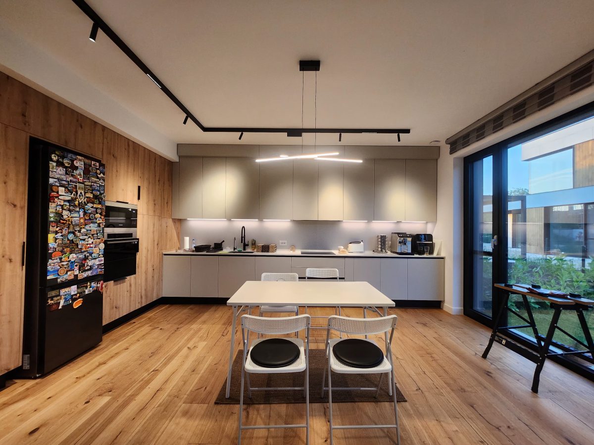 Modern kitchen with wooden wall panels, gray cabinets, and a white dining table in the foreground.