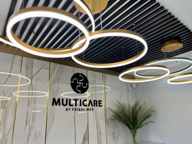 Interior of a modern clinic with gold circular ring chandeliers and marble wall panels, featuring the 'MULTICARE BY FRIEDL MED' sign.