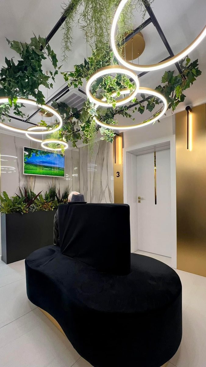 Modern lobby seating area with a curved black sofa, hanging greenery, and circular LED rings overhead; a white door labeled 3 in the background.
