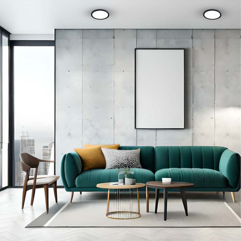 Modern living room with a teal velvet sofa, mustard and zebra-print pillows, and two round coffee tables in front of a concrete wall and large blank art frame.
