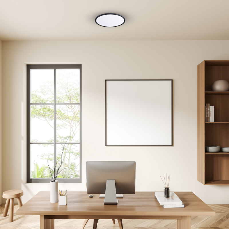 Minimalist home office: wooden desk with monitor, vase with branches, books, diffuser, and a large blank-framed wall art.
