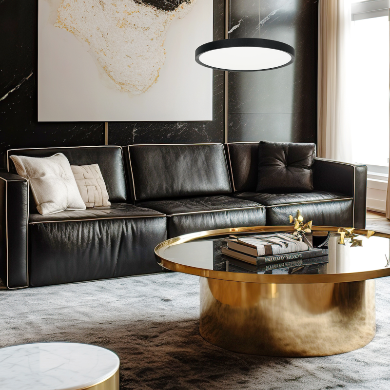 Modern living room with a black leather sectional, neutral pillows, and a round gold coffee table with books; abstract art on a dark wall above.