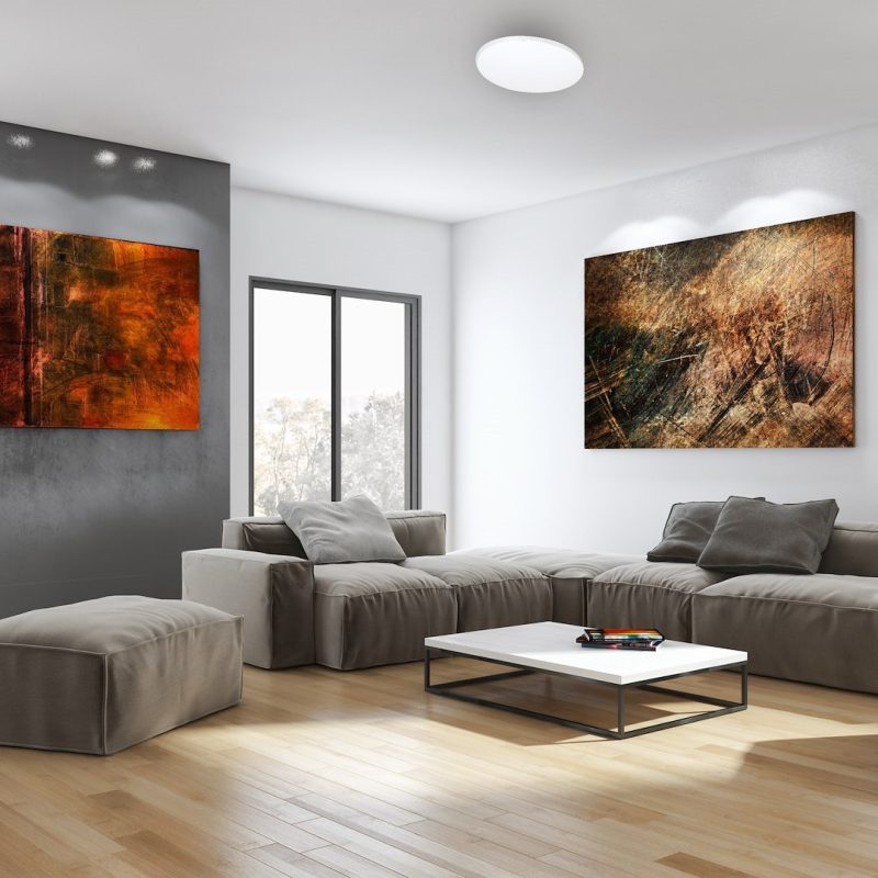 Modern living room with a beige sectional sofa, white coffee table, and two large abstract paintings on white and gray walls.