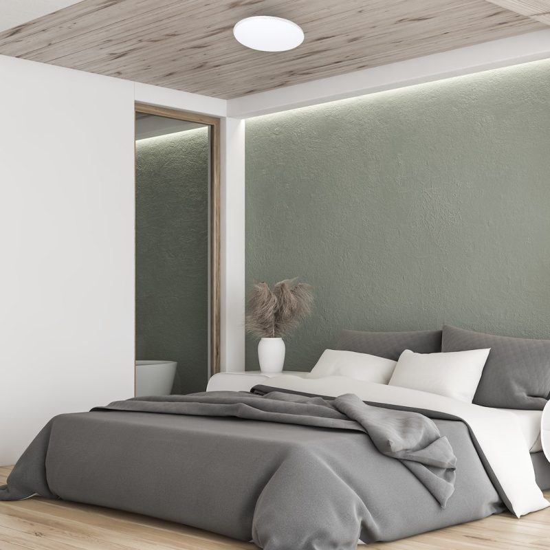 Modern bedroom with gray bedding and white pillows against a textured sage wall, wooden ceiling, and a white vase with dried pampas grass on the nightstand.