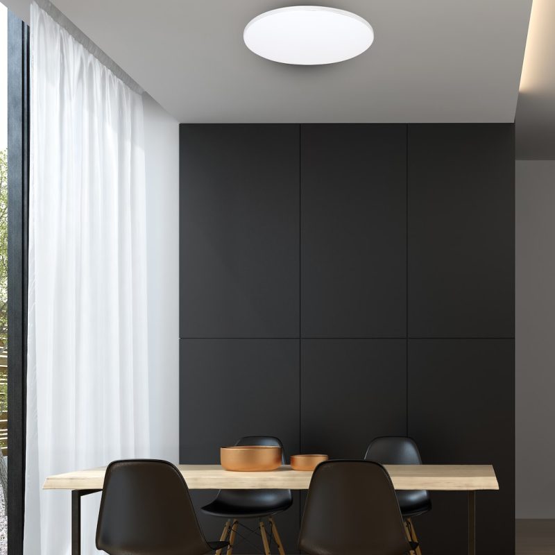 Minimalist dining room: black paneled wall, light wood table, four black chairs, copper bowls, white sheer curtains, and a circular ceiling light.