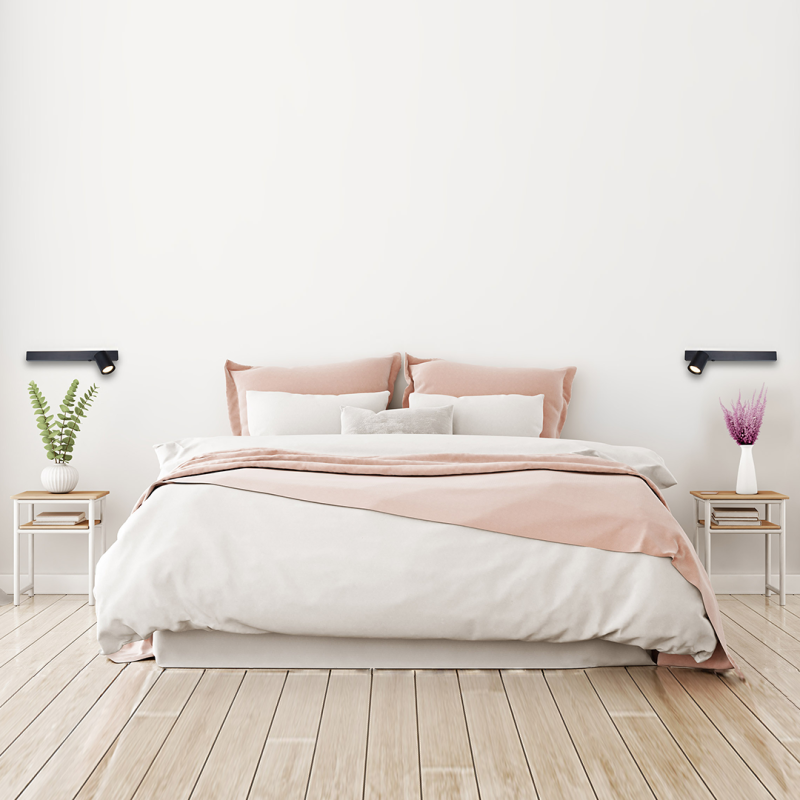 Minimalist bedroom with a blush-pink and white bed, two matching nightstands, and wall-mounted lights.