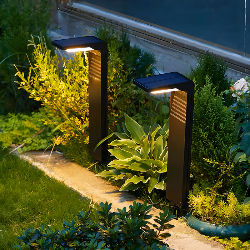Two black solar-powered garden lights along a stone path, illuminating greenery at dusk.