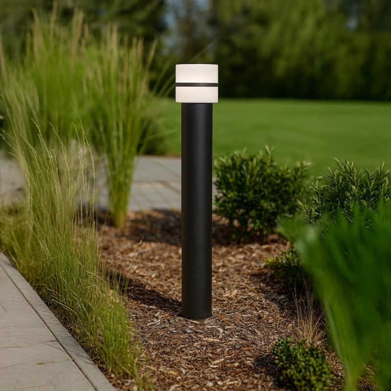 Outdoor bollard path light with a black post and white cap beside a mulch bed along a walkway