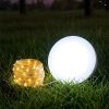 Glowing white sphere light beside a warm string-light coil on grass at dusk.