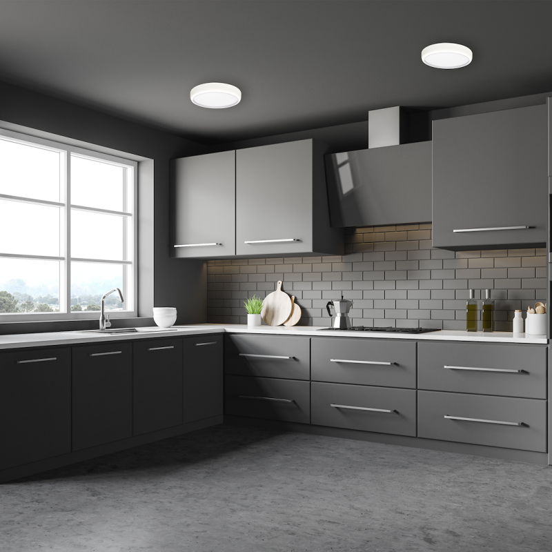 Modern gray L-shaped kitchen with white countertops, gray cabinets, and a subway-tile backsplash; window above the sink and a stove with a range hood on the right.