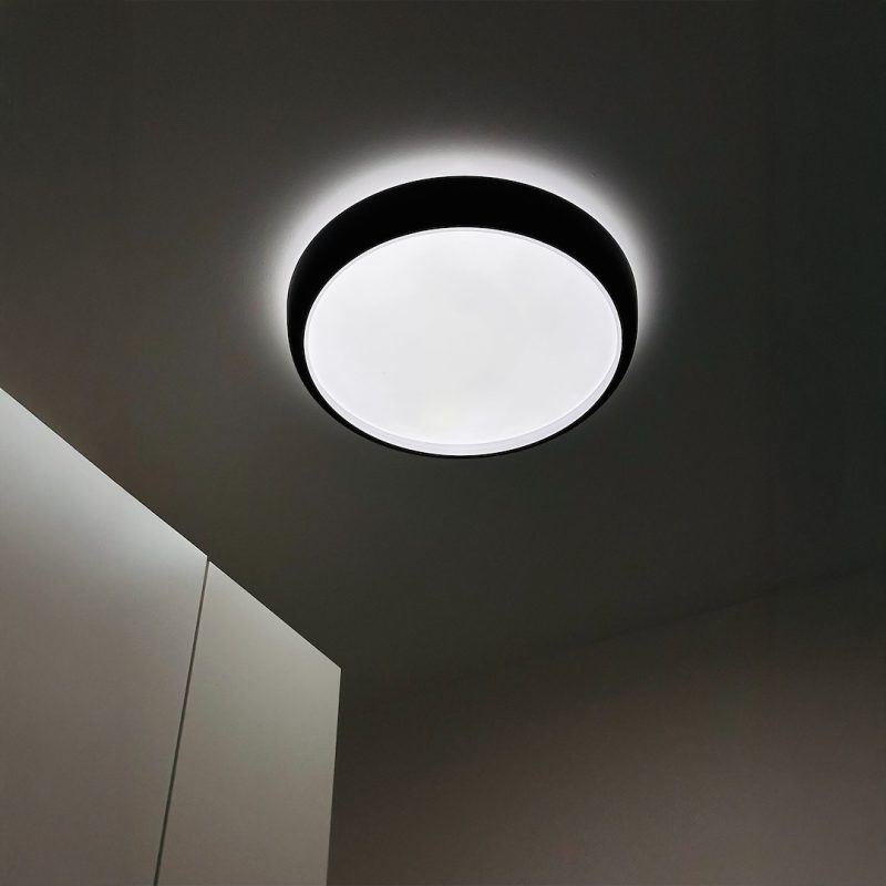 Circular ceiling light with a black rim and bright white diffuser casting a soft glow in a dim room