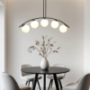 Minimalist dining nook with a round black table, four gray chairs, a white vase with branches, and a curved five-bulb ceiling light.