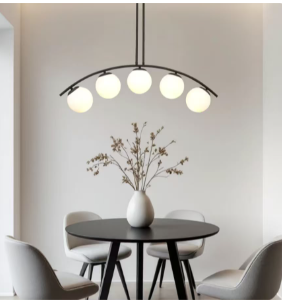 Minimalist dining nook with a round black table, four gray chairs, a white vase with branches, and a curved five-bulb ceiling light.