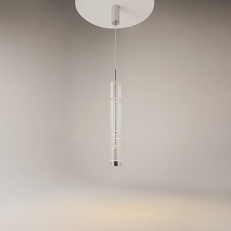Minimalist glass pendant light suspended from the ceiling, featuring stacked cylindrical glass sections and warm illumination