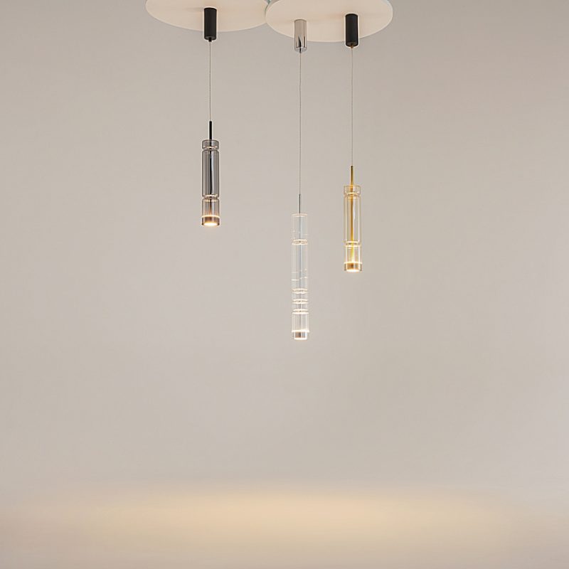 Three modern glass pendant lights hanging from the ceiling, casting warm light in a neutral room.