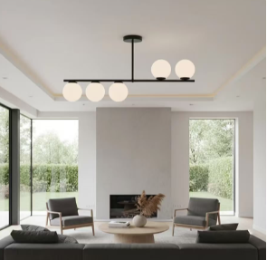 Modern living room with a central fireplace, round coffee table, gray seating, a black rod chandelier with globe lights, and large windows overlooking greenery.
