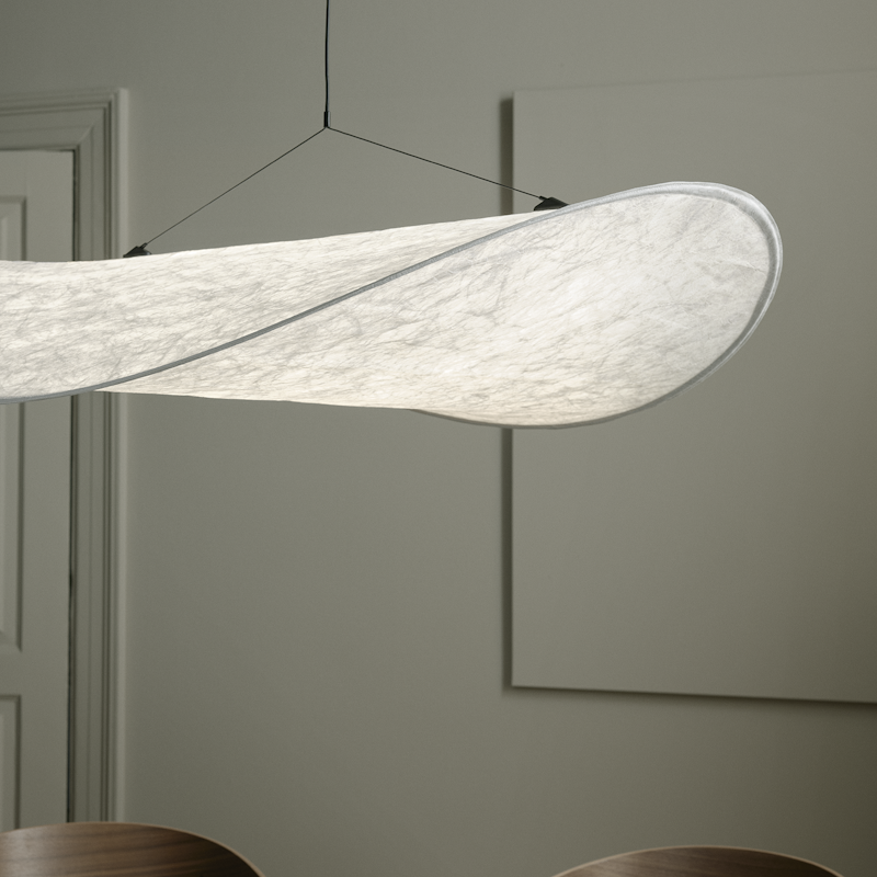 White curved fabric pendant light hanging from the ceiling over a dark round table in a gray-room, with wooden chairs nearby