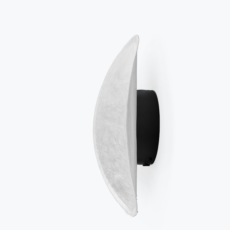 Side view of a crescent-shaped white wall lamp with a black circular mount (wall sconce).