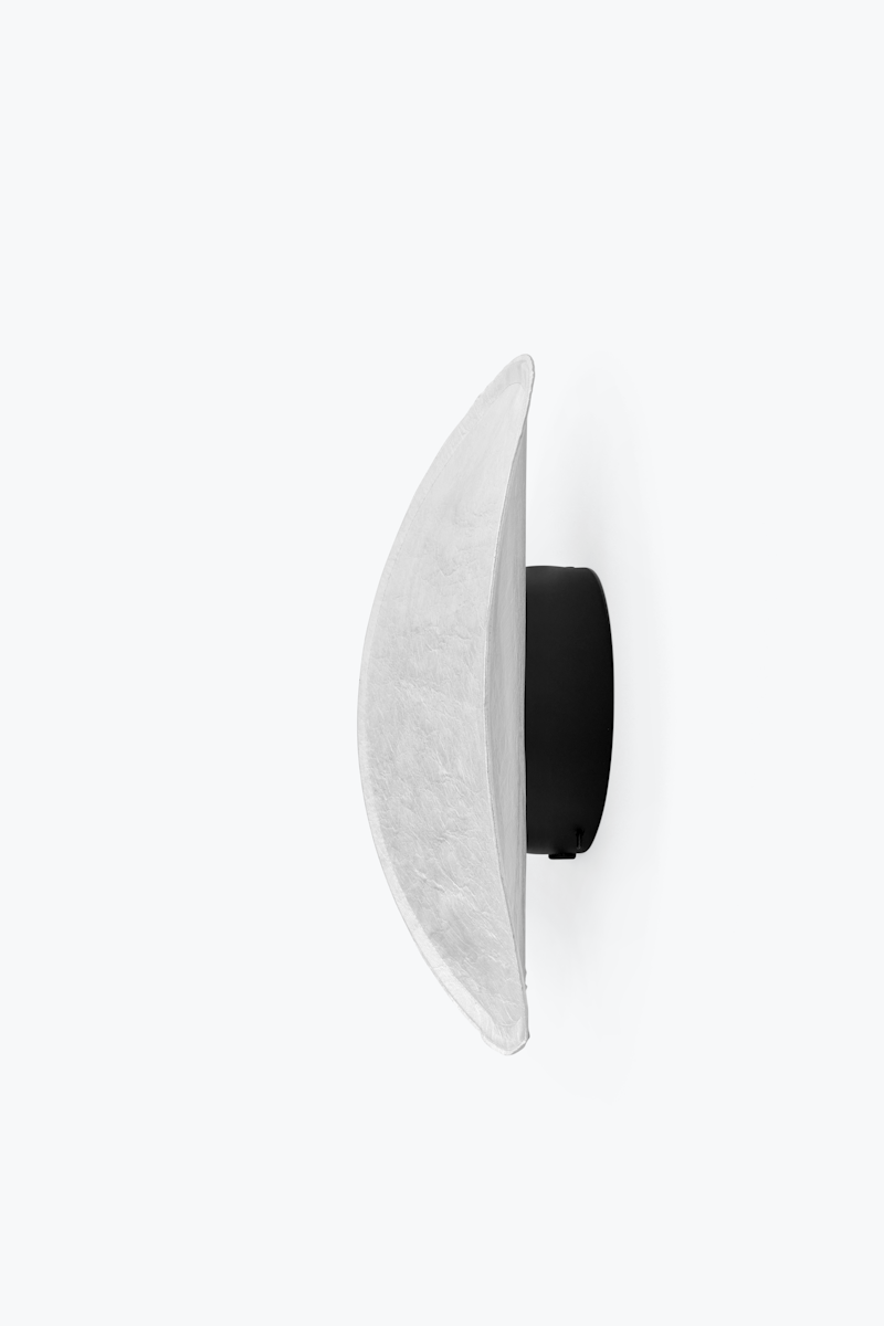 Side view of a crescent-shaped white wall lamp with a black circular mount (wall sconce).