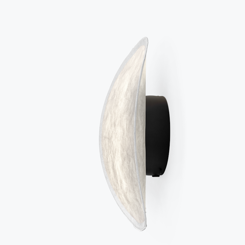 Side view of a wall-mounted circular fabric lampshade attached to a black backing on a white wall.