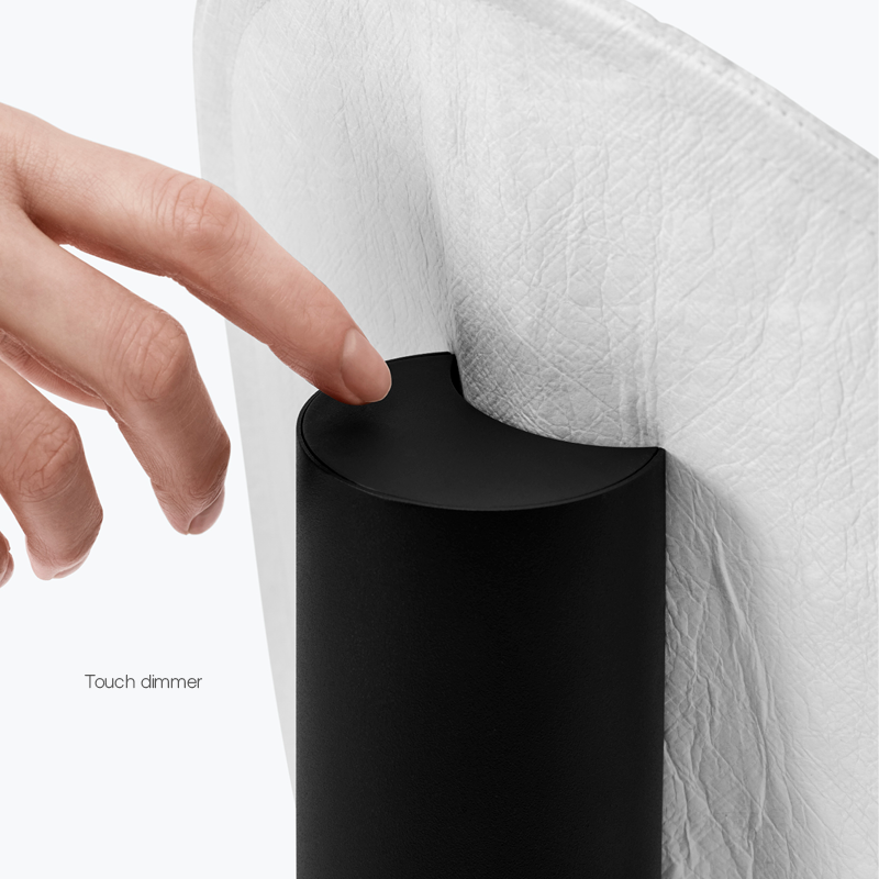 Close-up of a hand tapping a touch dimmer on a sleek black lamp near a white textured lampshade.