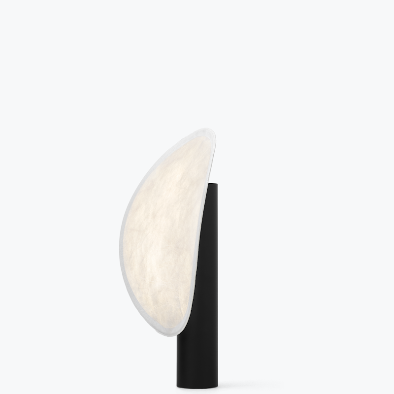 Side profile of a modern table lamp: a black cylindrical base with a curved beige fabric lampshade extending to the left