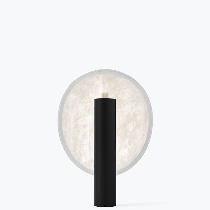 Minimalist black cylindrical lamp in front of a large round frosted light panel, modern accent lighting.