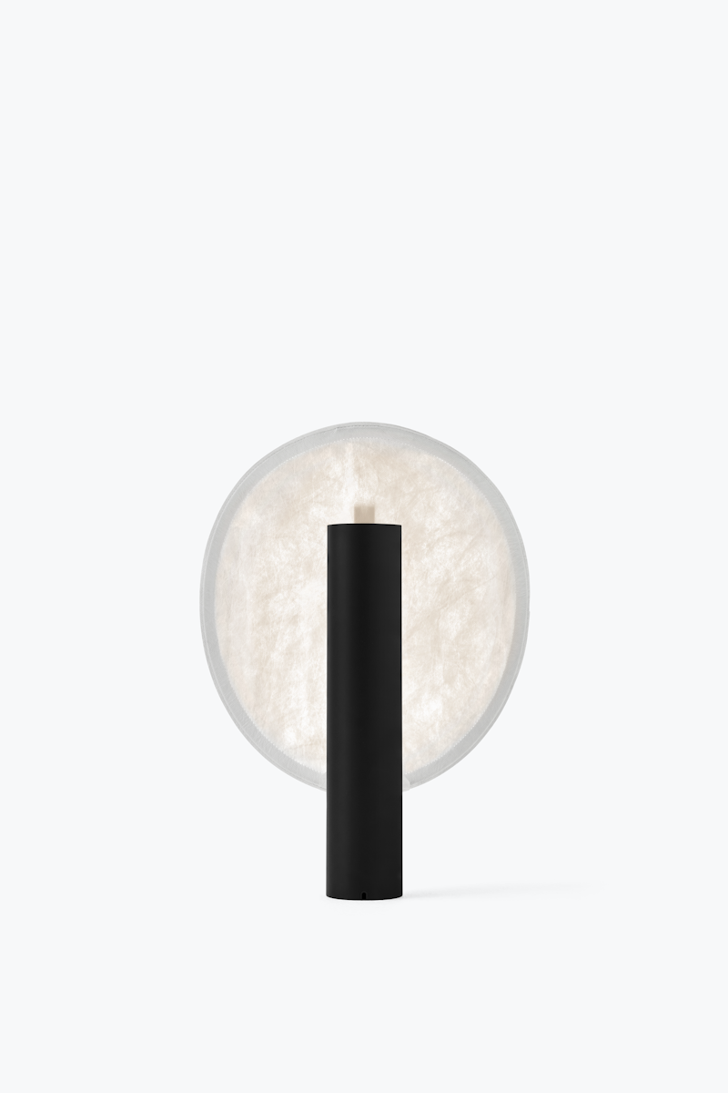 Minimalist black cylindrical lamp in front of a large round frosted light panel, modern accent lighting.