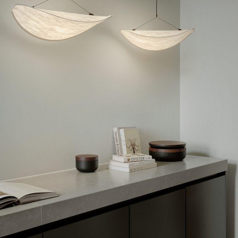 Minimalist kitchen console with stacked books and round wooden bowls on a marble countertop, two curved pendant lights above.