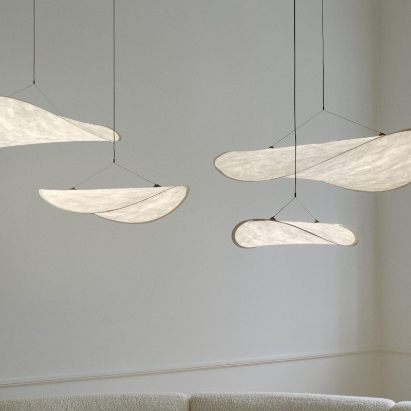 Minimalist living room with sculptural white fabric leaf pendants hanging from the ceiling above a cream sectional sofa.