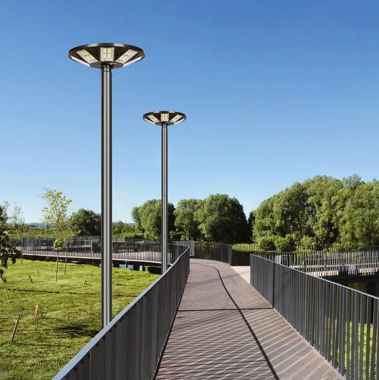 Elevated pedestrian walkway with metal railings and two tall solar-powered street lamps beside a grassy park under a clear blue sky.