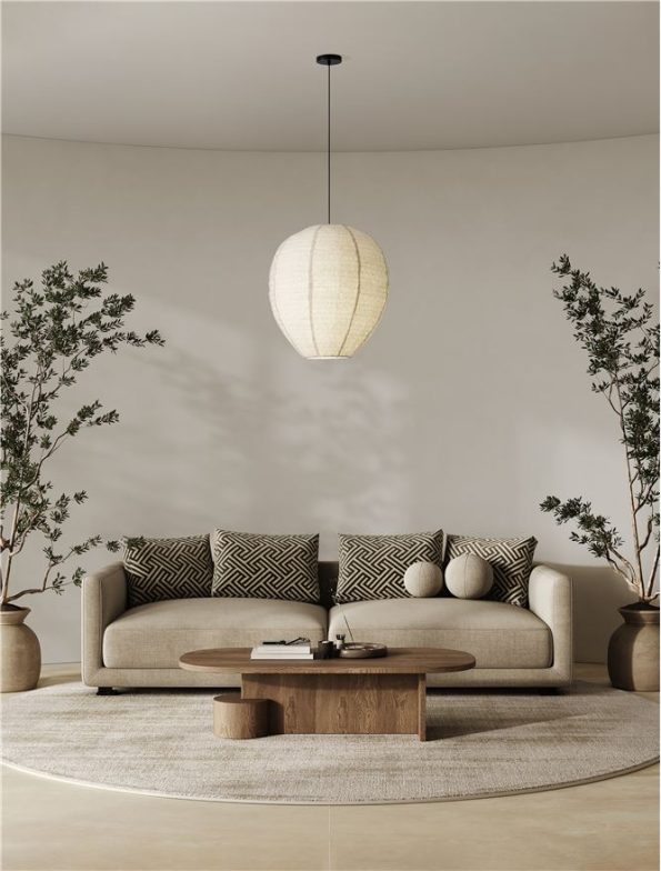 Neutral living room featuring a beige sofa, geometric cushions, round wooden coffee table, potted trees, and a hanging pendant light.