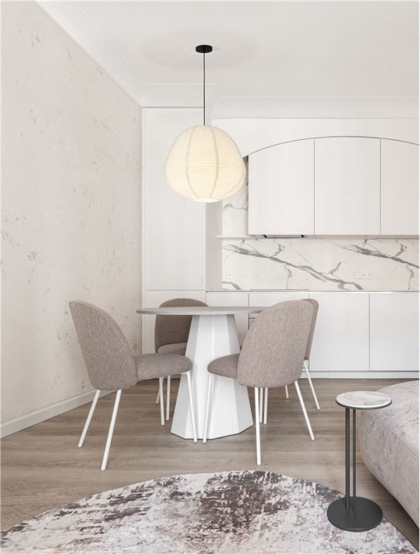 Bright white kitchen with marble backsplash, round pedestal dining table and four beige chairs under a pendant lamp.