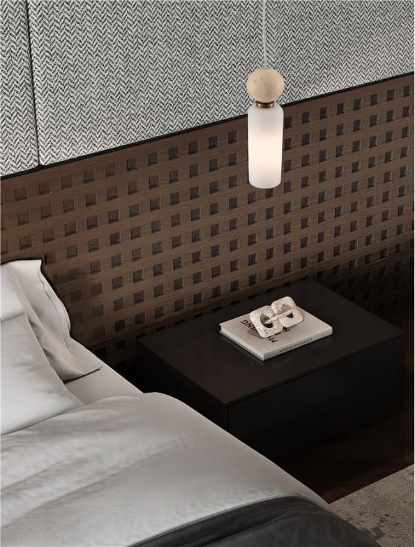 Hotel-style bedroom corner: bed, black nightstand, white wall lamp, and a book with a silver sculpture on top of the nightstand.