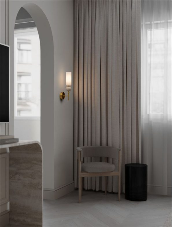 Neutral-toned living room corner with a wooden chair, black drum side table, tall sheer curtains, and an arched doorway with a wall sconce.