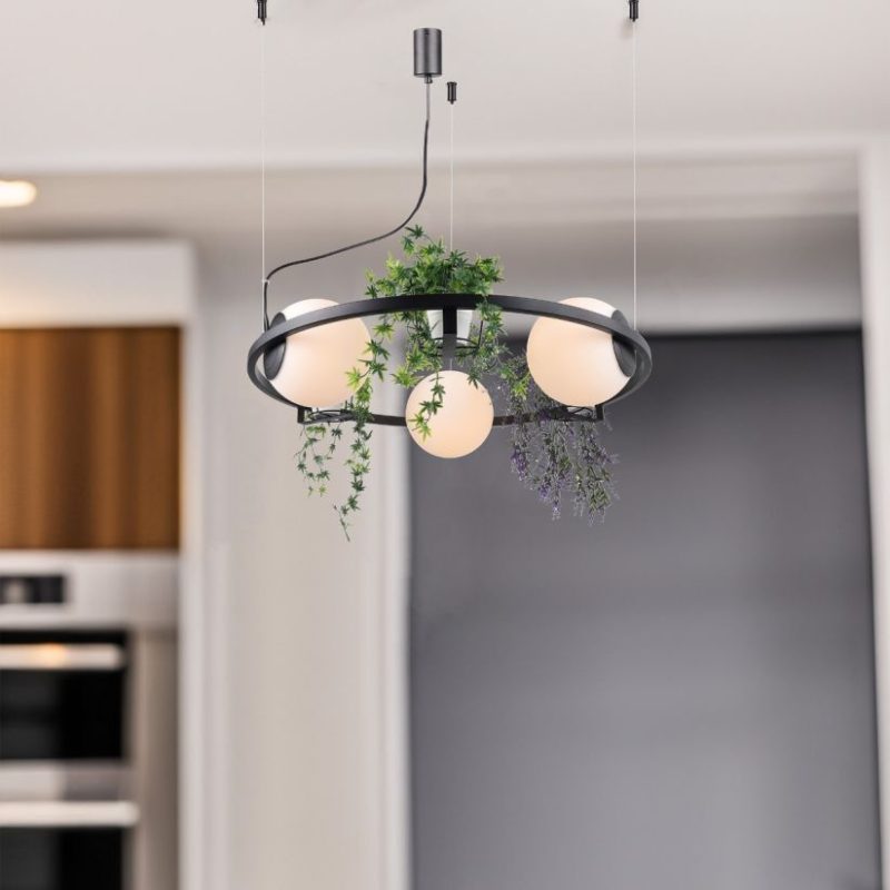 Modern black circular pendant light with four frosted globe bulbs and trailing greenery around the frame.