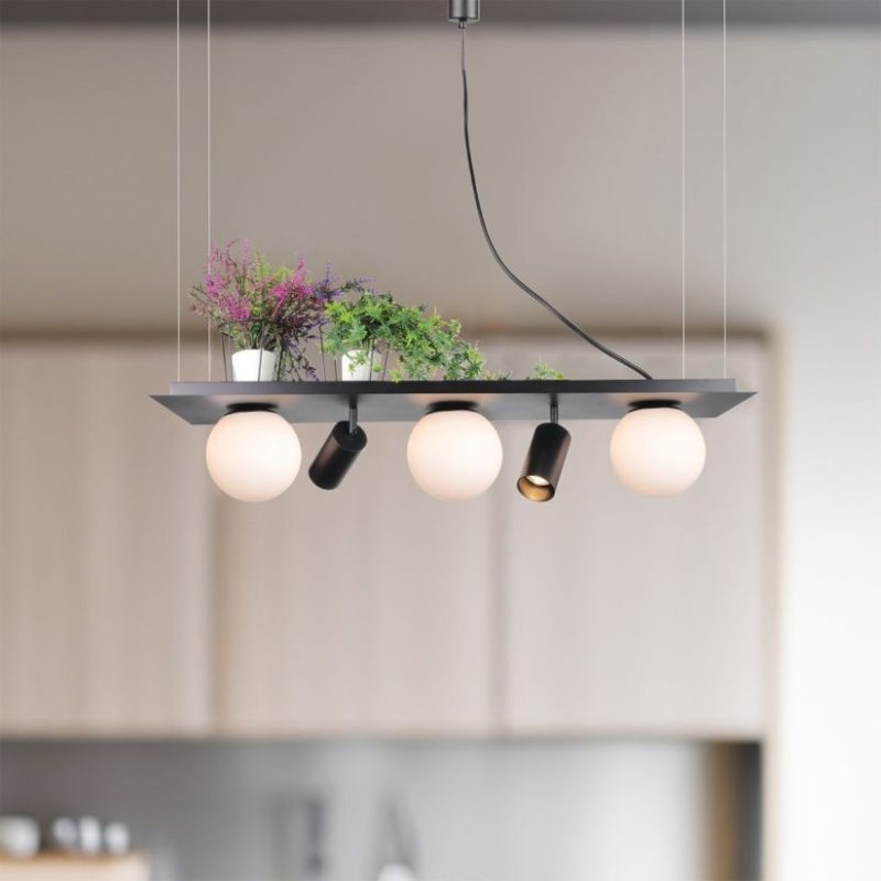 Modern ceiling pendant light with four bulbs and two black spotlights, greenery on top, hanging over a kitchen area.