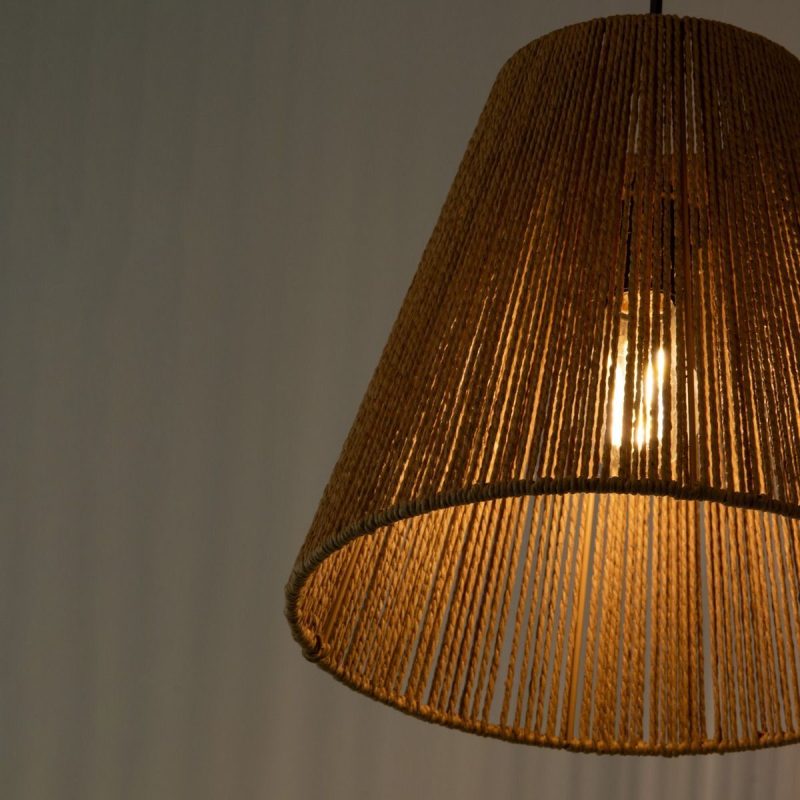 Woven wicker lampshade with a lit bulb glowing from inside.