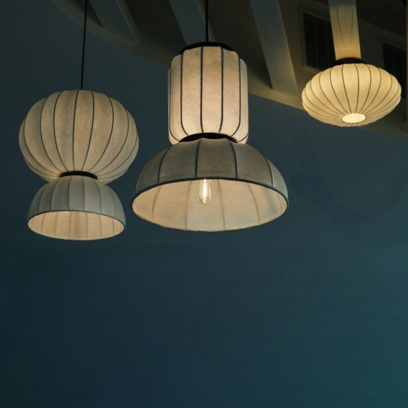 Three white fabric pendant lamps with vertical pleats hang from the ceiling over a blue wall, creating soft ambient lighting.