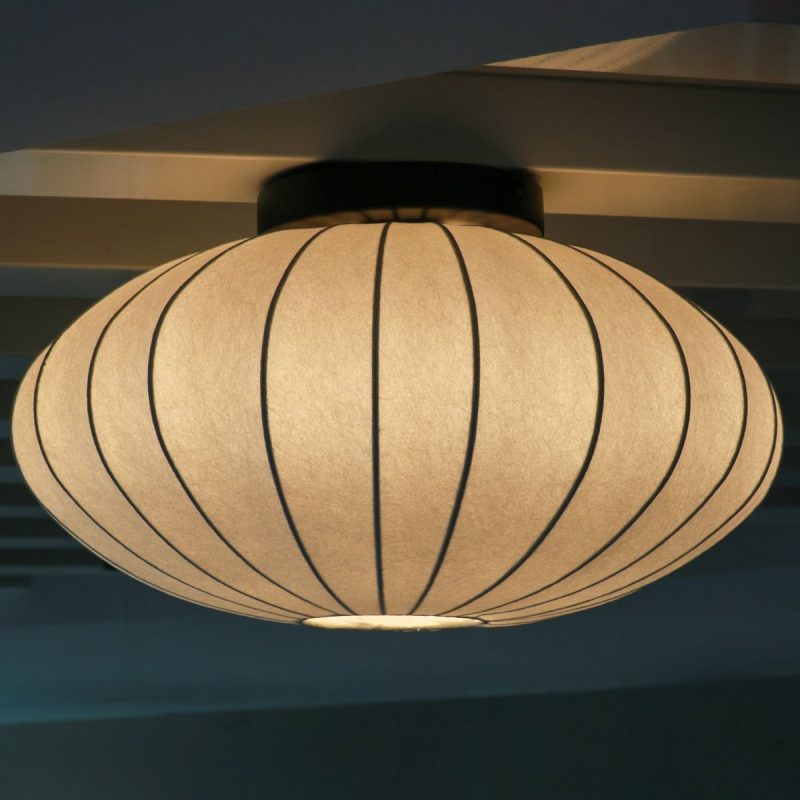 Round white paper lantern ceiling light with vertical black ribs, glowing softly.