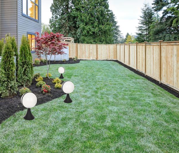 Backyard with a green lawn, a flower bed along the house, round globe lights on black pedestals, and a wooden privacy fence far back in the yard.