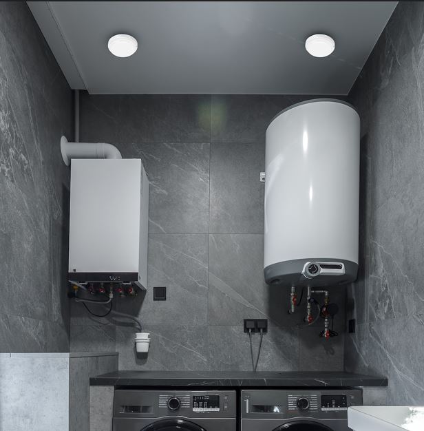 Utility room with a wall-mounted boiler, a tall white water heater, and two front-loading washing machines beneath a dark tiled wall.