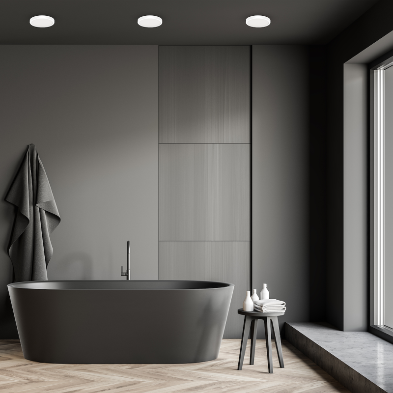 Dark gray freestanding bathtub in a minimalist bathroom with a wood herringbone floor and a large window to the right.