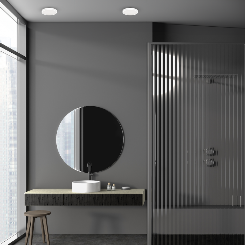 Modern gray bathroom with a round mirror above a concrete floating vanity, white vessel sink, black faucet, and a glass-walled shower with vertical stripes.
